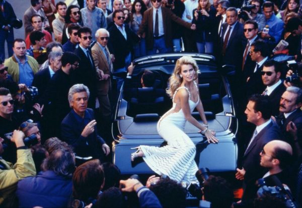 Claudia Schiffer for Valentino by Arthur Elgort, the model in white sitting on a car between men in suits