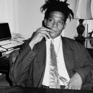 Jean Michel Basquiat by Roxanne Lowit, the artist in a suit and silk tie, smoking
