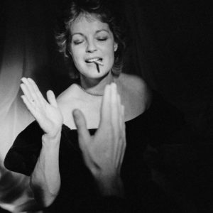Romy Schneider by Arthur Elgort, the actress in a black dress smoking and giving a high fiive