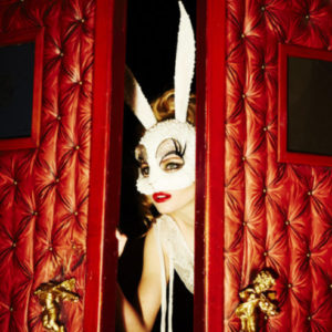 peeking bunny by ellen von unwerth, model in crystal bunny mask behind red cushion doors