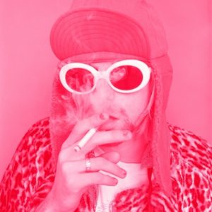 Kurt Cobain Smoking by Jesse Frohman, portrait of the singer in hat and sunglasses, pink