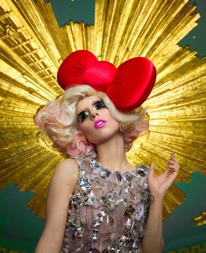 Lady Gaga with red bow by Markus Klinko, the singer with cartoonish makeup and red bow in front of golden halo