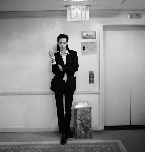 Nick Cave by Jesse Frohman, the musician in a black suit smoking next to a hotel elevator