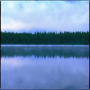 Montana 22 by Nigel Parry, Lake and trees reflecting in the water with cloudy sky