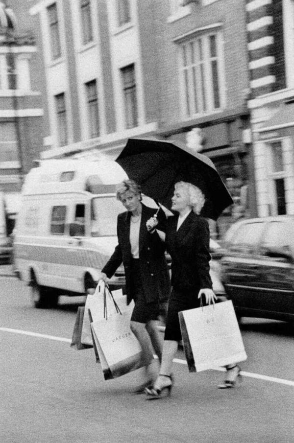 Marilyn and Diana Shopping by Alison Jackson, black-and-white fine art photography of two doubles crossing the street with shopping bags holding an umbrella
