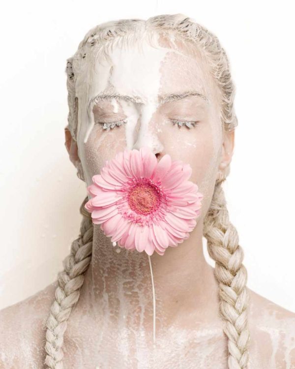 "Flower Girl, 2016" by Sylvie Blum, part of the Space Age Series. Fine Art Print, colour, showing woman with flower in mouth, braided hair and eyes closed, milk running across her face