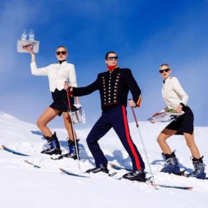 "Room Service" by Tony Kelly, Colour fine art print showing three staff with champagne on the slope wearing skiers