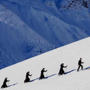 "Saint Moritz, St. Moritz, Switzerland, 2024" by Tony Kelly. Colour fine art print showing nuns climbing a mountain in skis. White snow and blue-lit mountain background.
