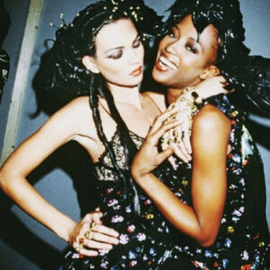 Kate Moss and Naomi Campbell backstage by Roxanne Lowit - two models in flower dresses and headpieces hugging
