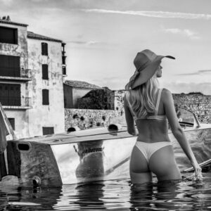 St. Tropez by David Yarrow - Moel in white Bikini standing in Water with a small motorboat.