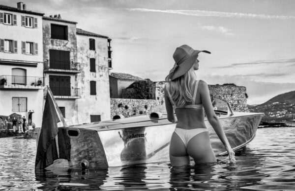 St. Tropez by David Yarrow - Moel in white Bikini standing in Water with a small motorboat.