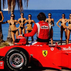 Pit Stop 2024 by Tony Kelly, Formula one driver on his red Ferrari Race Car looking at Models standing by the beach.