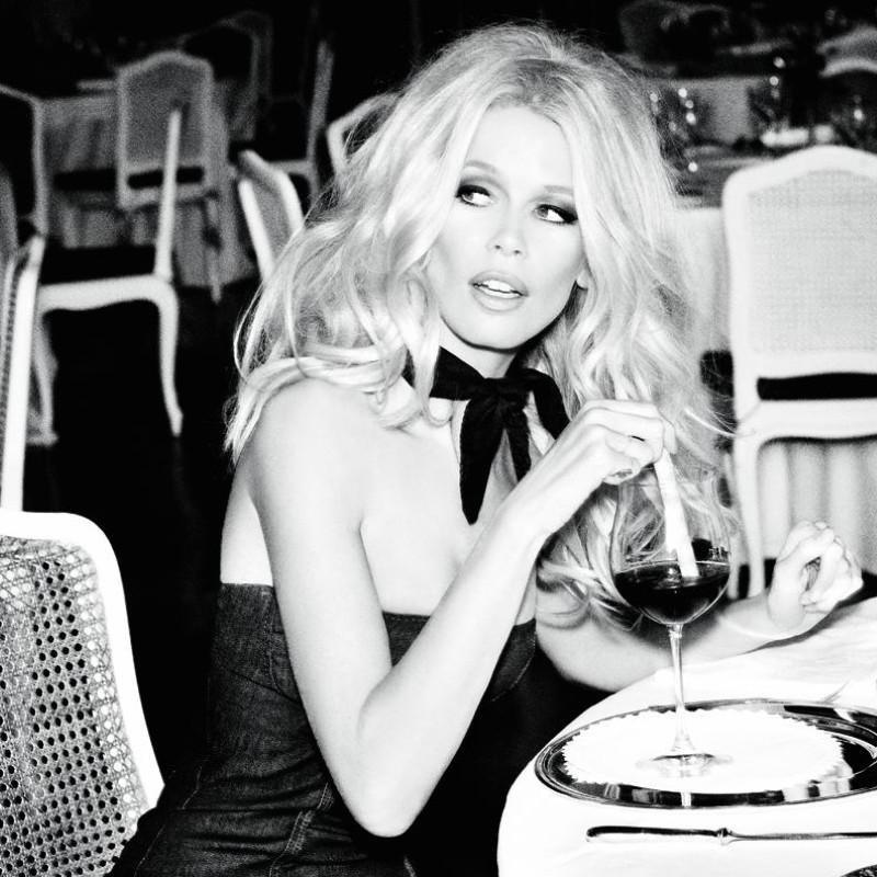 Claudia Schiffer for the 30th Guess anniversery by Ellen von Unwerth, the model in a black dress in a restaurant with a glass of wine