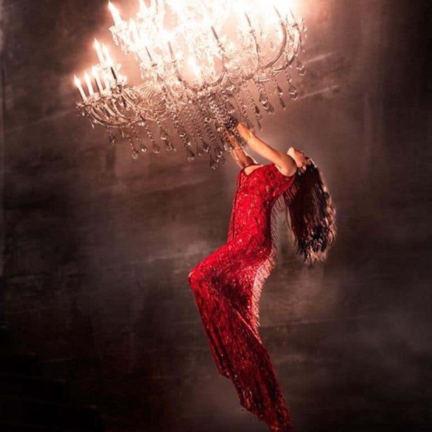 Hanging on by David Drebin, model in a red dress hanging from a chandelier